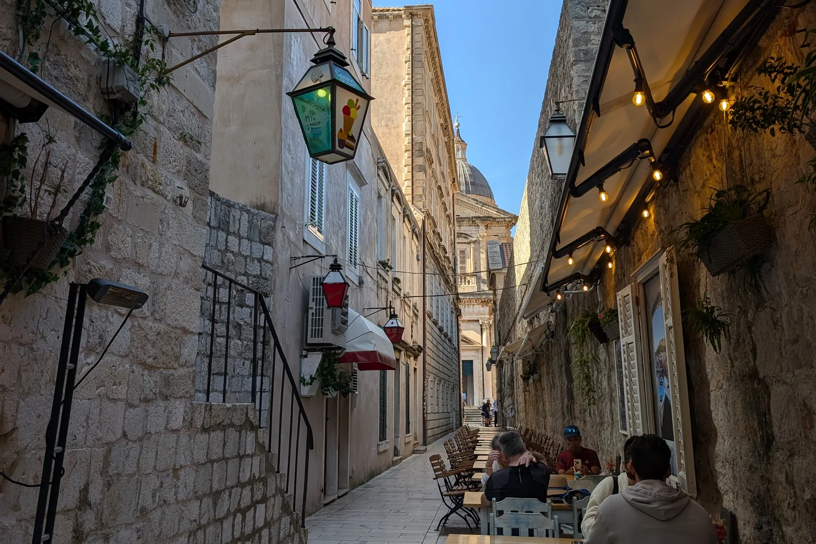 Cafe tables under lanterns in a Dubrovnik lane, the cathedral dome beyond
